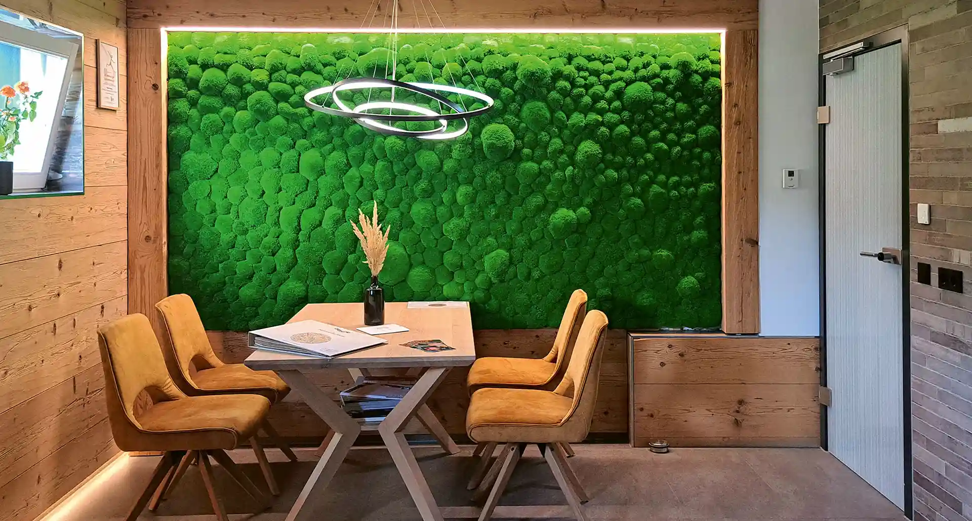 Große, sattgrüne Mooswand in einem gemütlichen Essbereich mit Holzelementen und modernen Stühlen, sorgt für ein natürliches Ambiente und eine ruhige Atmosphäre.