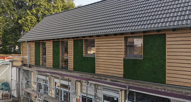Gebäude mit Holzverkleidung und integrierten Greenovation Mooswand-Elementen – ökologische Fassadengestaltung