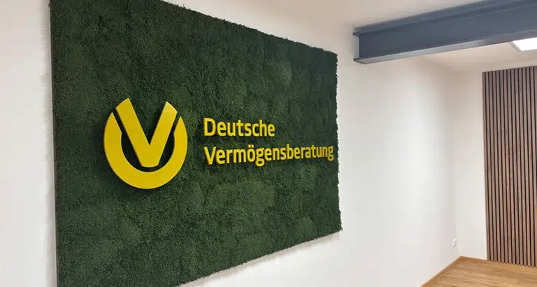 Mooswand mit gelbem Logo der Deutschen Vermögensberatung an Büroinnenwand