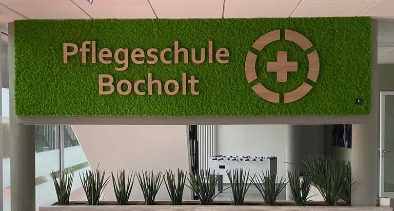 Grüne Mooswand mit Logo der Pflegeschule Bocholt im Eingangsbereich